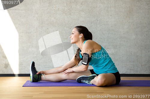 Image of smiling woman stretching leg on mat in gym