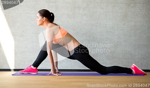 Image of smiling woman stretching leg on mat in gym