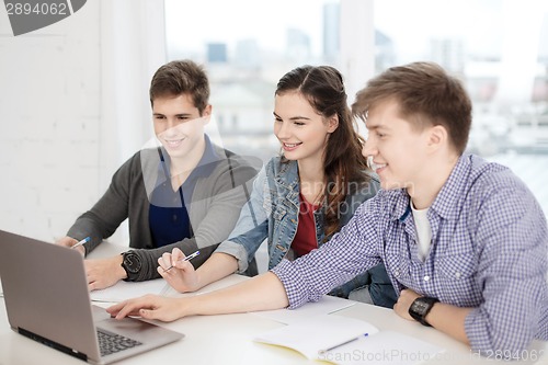 Image of three smiling students with laptop and notebooks