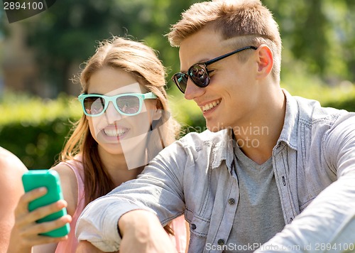 Image of smiling friends with smartphone sitting in park