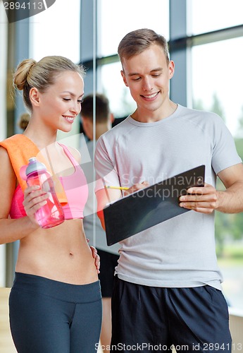 Image of smiling young woman with personal trainer in gym