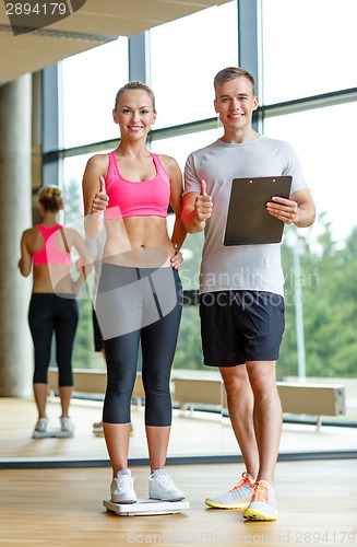 Image of smiling man and woman with scales in gym