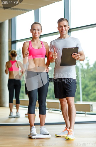 Image of smiling man and woman with scales in gym