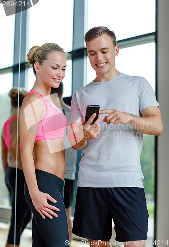 Image of smiling young woman with personal trainer in gym