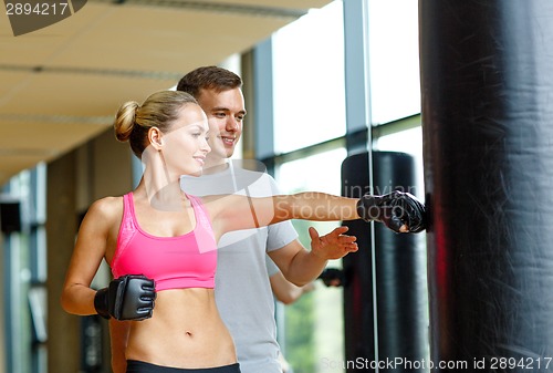 Image of smiling woman with personal trainer boxing in gym