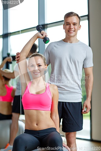 Image of smiling young woman with personal trainer in gym