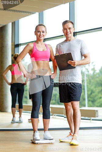 Image of smiling man and woman with scales in gym