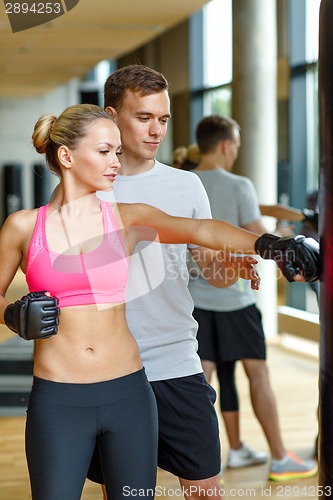 Image of smiling woman with personal trainer boxing in gym