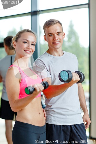 Image of smiling young woman with personal trainer in gym