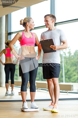 Image of smiling man and woman with scales in gym