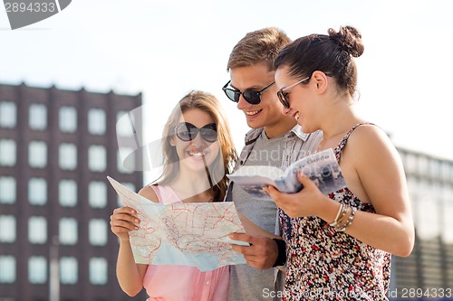 Image of smiling friends with map and city guide outdoors