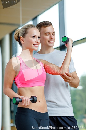 Image of smiling young woman with personal trainer in gym