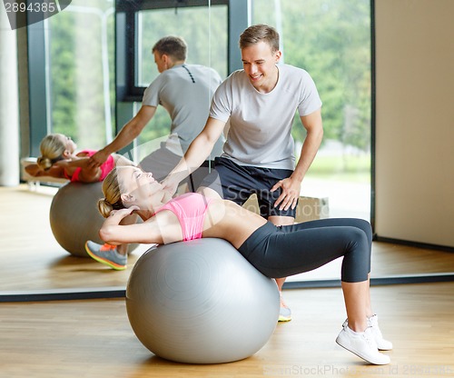 Image of smiling young woman with personal trainer in gym