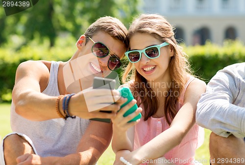 Image of smiling friends with smartphones sitting in park