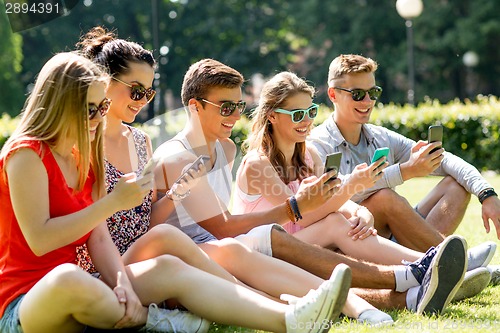 Image of smiling friends with smartphones sitting on grass