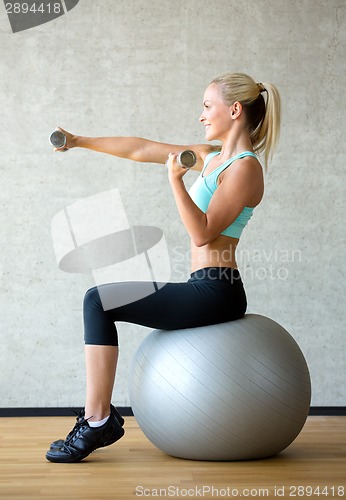 Image of smiling woman with dumbbells and exercise ball