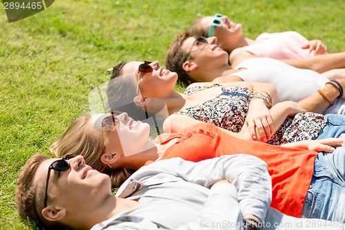 Image of group of smiling friends lying on grass outdoors