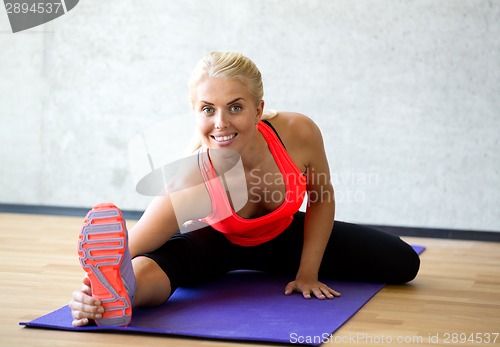 Image of smiling woman doing exercises on mat in gym