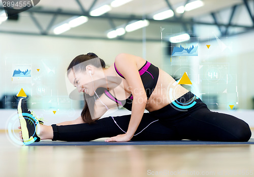 Image of smiling young woman stretching on mat in gym