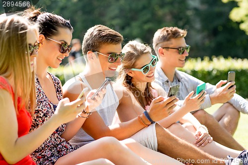 Image of smiling friends with smartphones sitting on grass