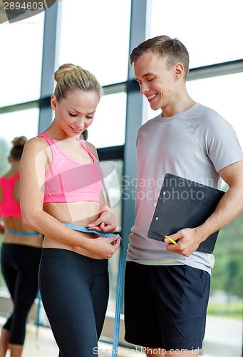 Image of smiling young woman with personal trainer in gym