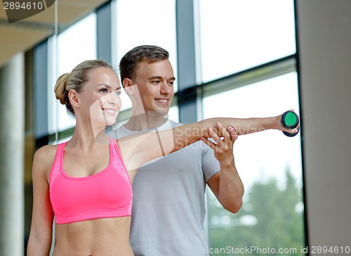 Image of smiling young woman with personal trainer in gym