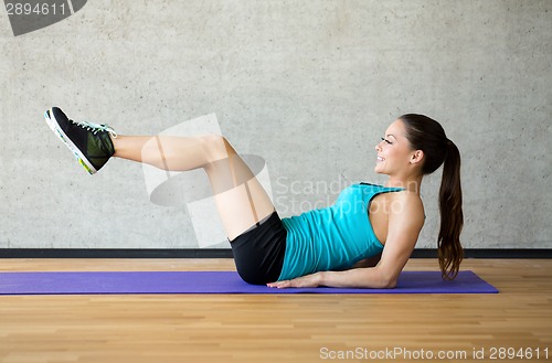 Image of smiling woman doing exercises on mat in gym