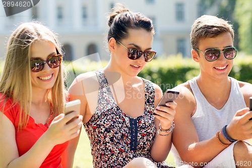 Image of smiling friends with smartphones sitting on grass