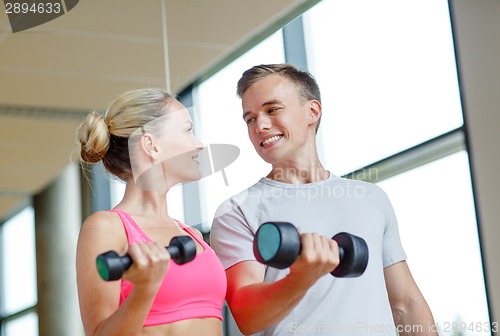 Image of smiling young woman with personal trainer in gym