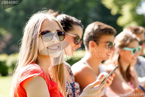 Image of smiling friends with smartphones sitting in park