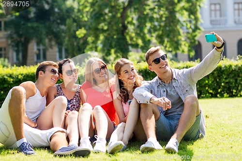 Image of smiling friends with smartphone sitting on grass
