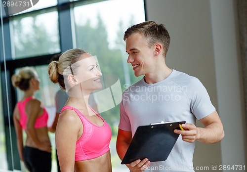 Image of smiling young woman with personal trainer in gym