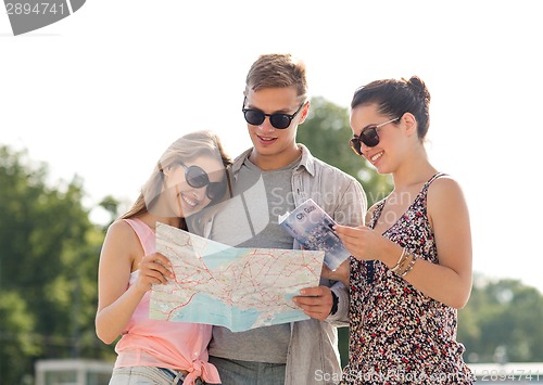 Image of smiling friends with map and city guide outdoors