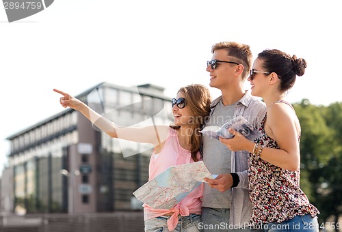 Image of smiling friends with map and city guide outdoors