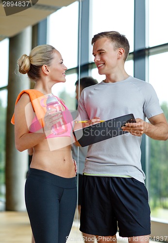 Image of smiling young woman with personal trainer in gym