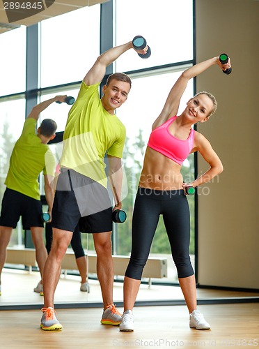 Image of smiling man and woman with dumbbells in gym