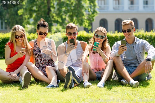 Image of smiling friends with smartphones sitting on grass