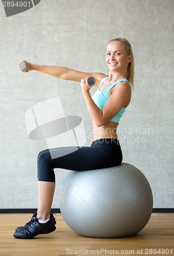 Image of smiling woman with dumbbells and exercise ball