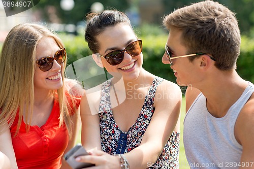 Image of smiling friends with smartphone sitting in park