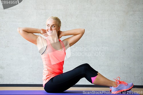 Image of smiling woman doing exercises on mat in gym