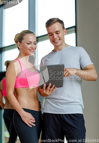 Image of smiling young woman with personal trainer in gym