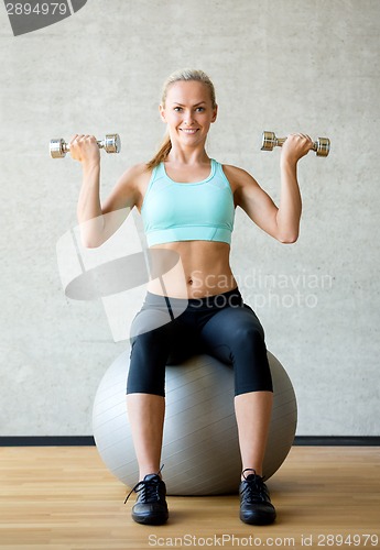 Image of smiling woman with dumbbells and exercise ball