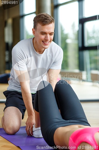 Image of smiling woman with male trainer exercising in gym