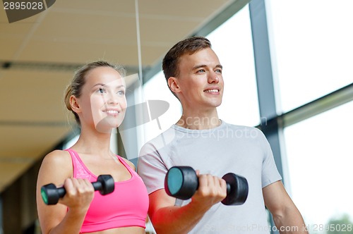 Image of smiling young woman with personal trainer in gym