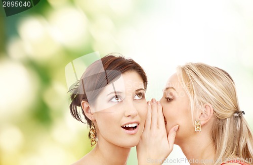 Image of two smiling women whispering gossip