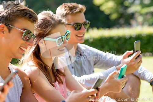 Image of smiling friends with smartphones sitting on grass