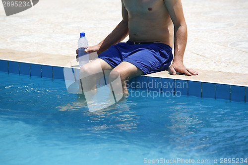 Image of Attractive man with blue swimsuit and a bottle of water enjoys s