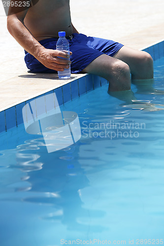 Image of Attractive man with blue swimsuit and a bottle of water enjoys s