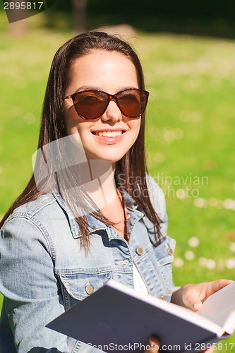 Image of smiling young girl with book sitting in park