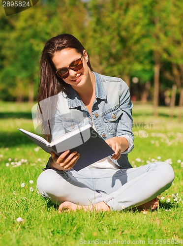 Image of smiling young girl with book sitting in park